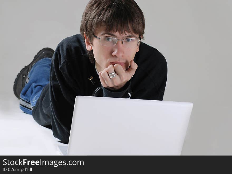 A guy with a laptop is lying on the floor and looking at the camera