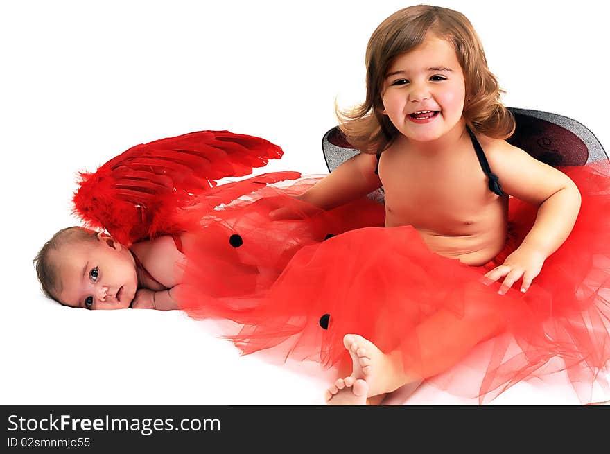 Two sisters playing and smiling in studio wearing red angle wings