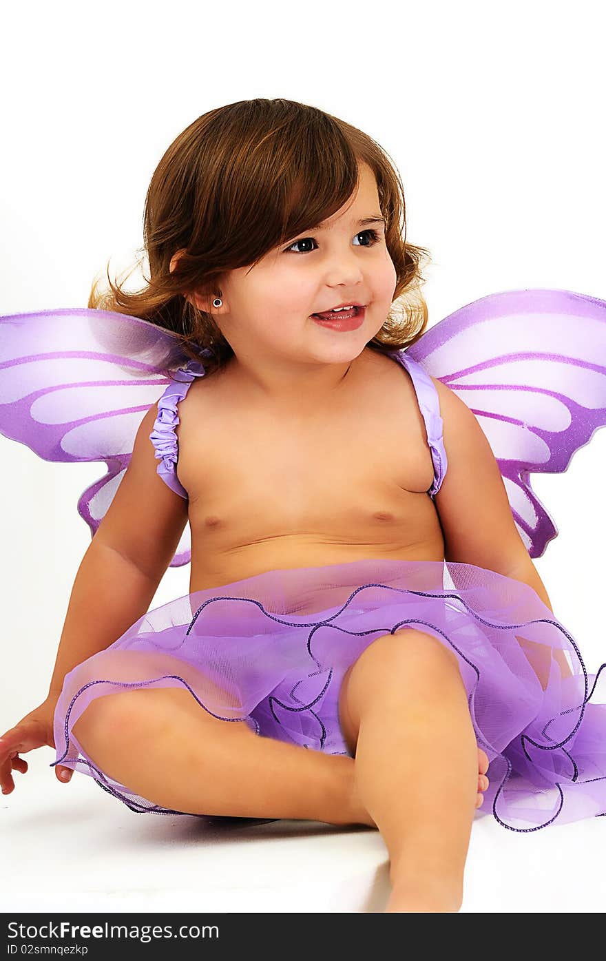 Little girl with purple angle wings sitting in studio and smiling. Little girl with purple angle wings sitting in studio and smiling