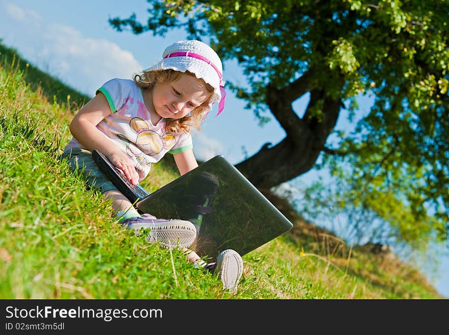 Little girl with laptop outside on grass