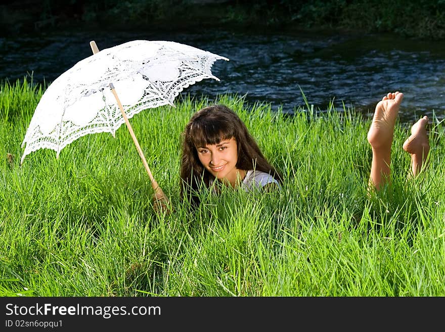 Young  beautiful girl  with sun umbrella relaxing in the fresh green grass near the river. Young  beautiful girl  with sun umbrella relaxing in the fresh green grass near the river