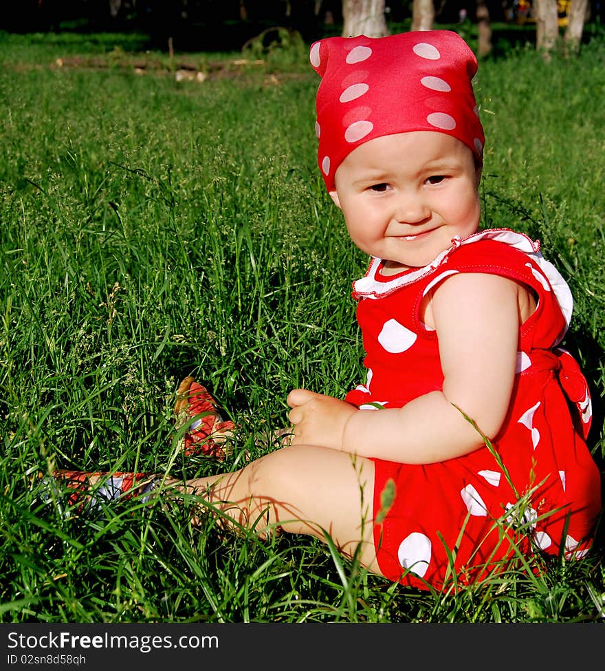 Baby is a red and white dress sitting on the grass. Baby is a red and white dress sitting on the grass