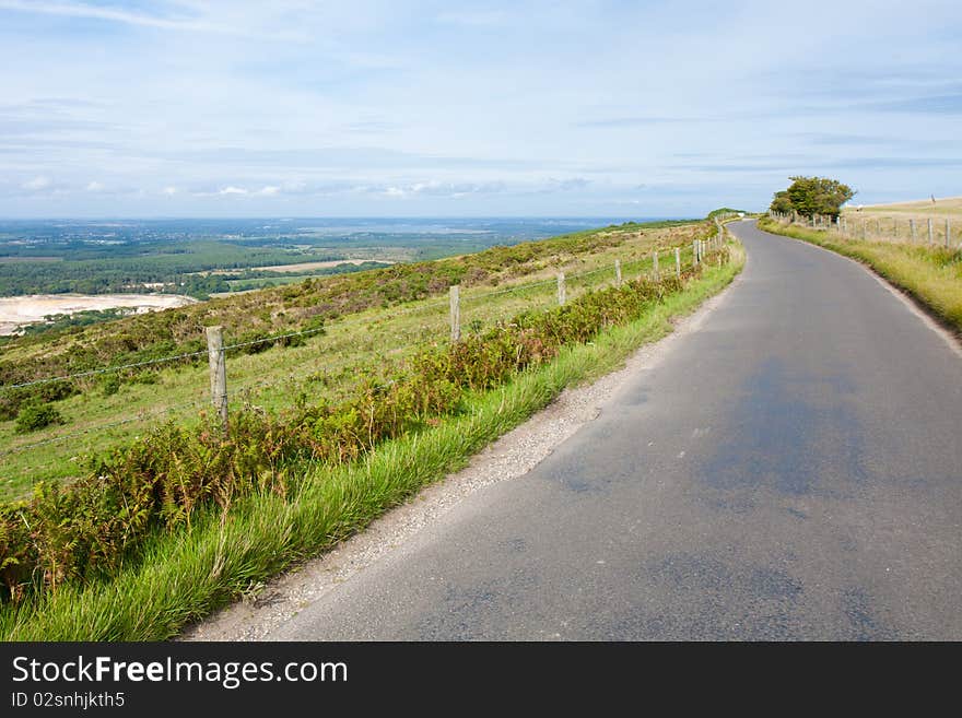 A road winds around the edge of the top of a hill in England on a cloudy summer afternoon. A road winds around the edge of the top of a hill in England on a cloudy summer afternoon.