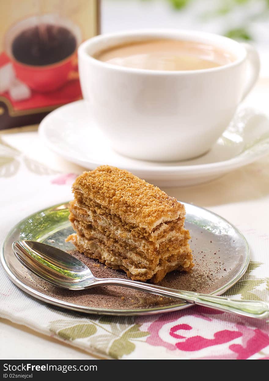 Slice of honey cake on a plate with cherry and coffee in background. Slice of honey cake on a plate with cherry and coffee in background.