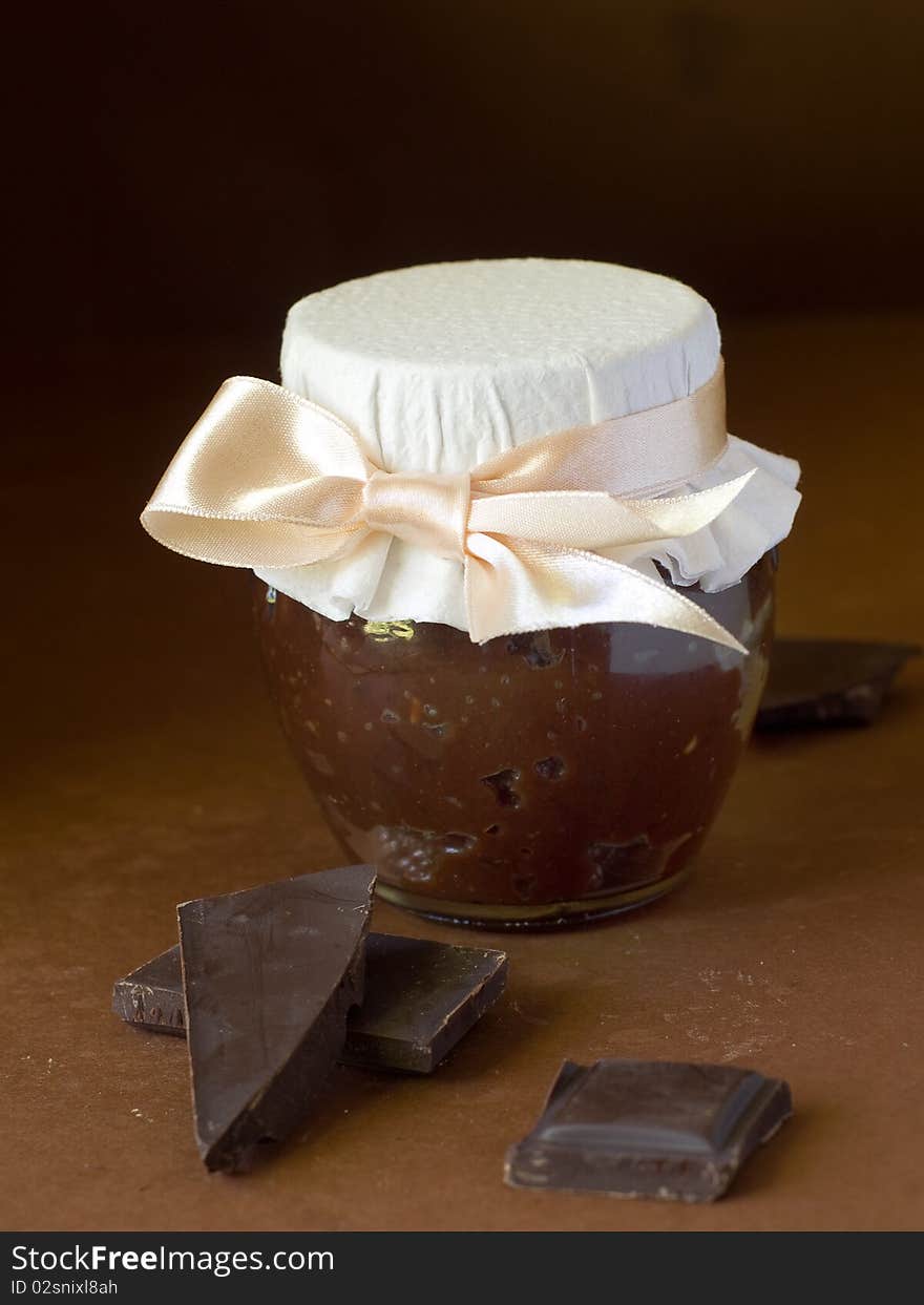 Chocolate marmalade in jar with ribbon on brown background