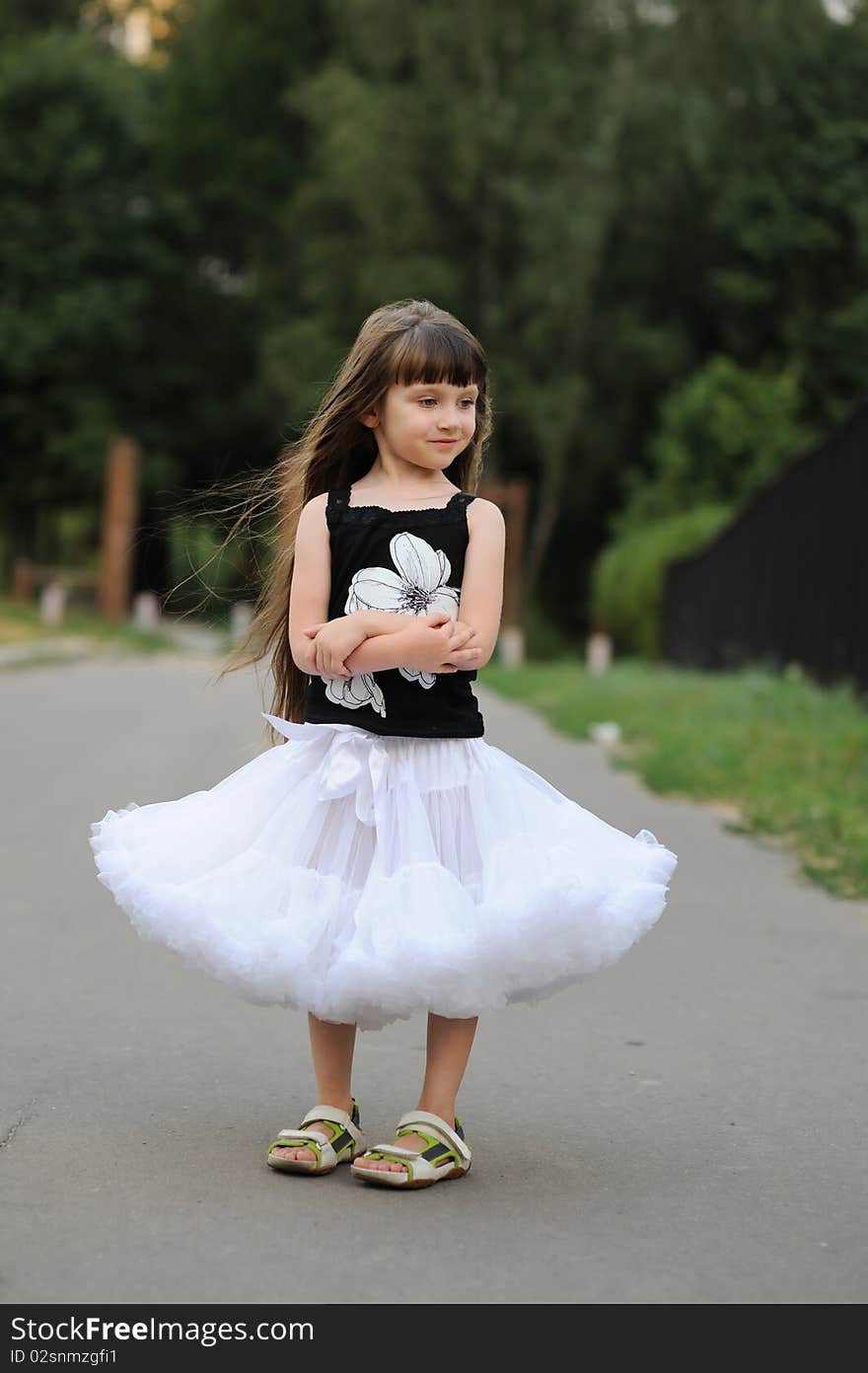 Adorable toddler girl with very long dark hair on the road in white tutu skirt