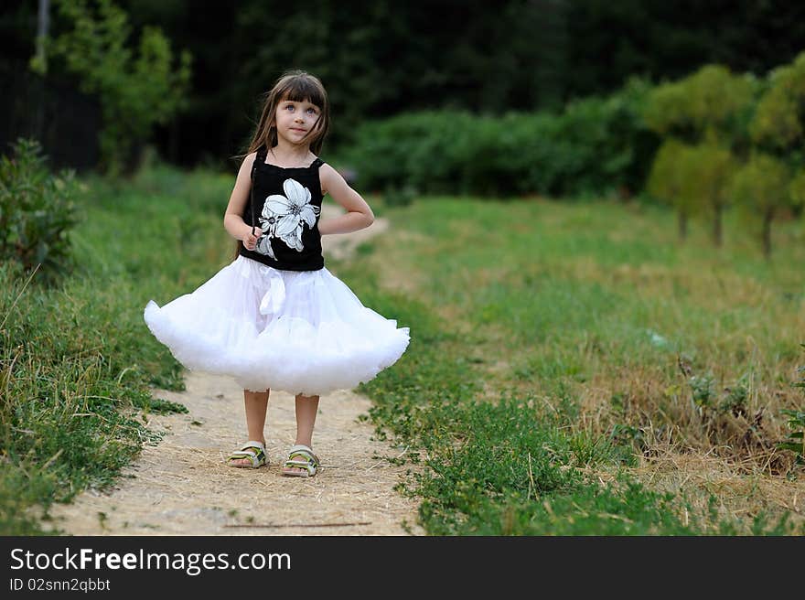 Adorable toddler girl in white tutu skirt with very long dark fluttering hair on country road. Adorable toddler girl in white tutu skirt with very long dark fluttering hair on country road