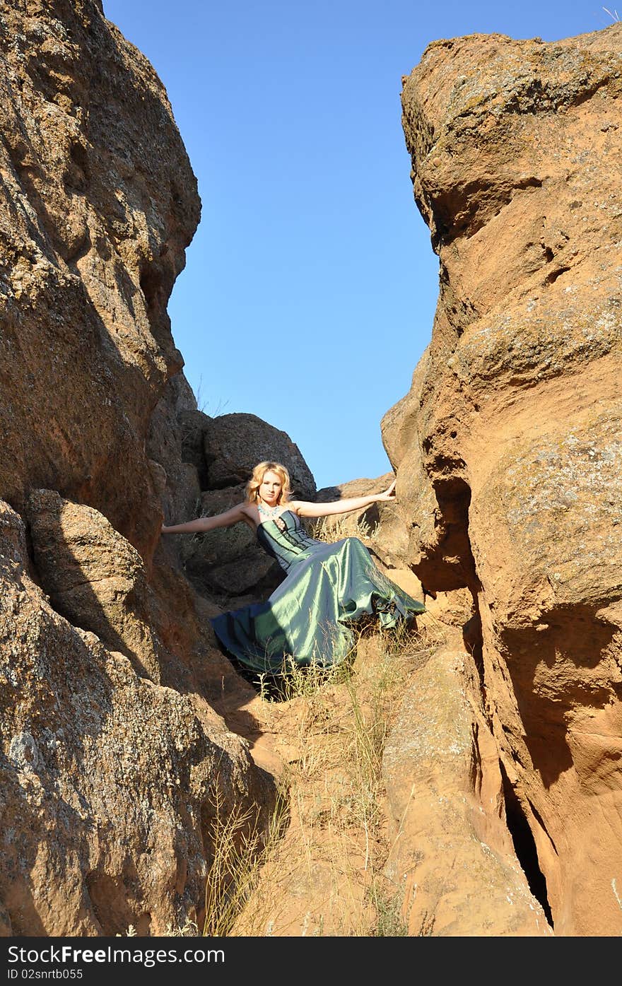 Attractive woman in long green dress siting in the stony ravine. Attractive woman in long green dress siting in the stony ravine