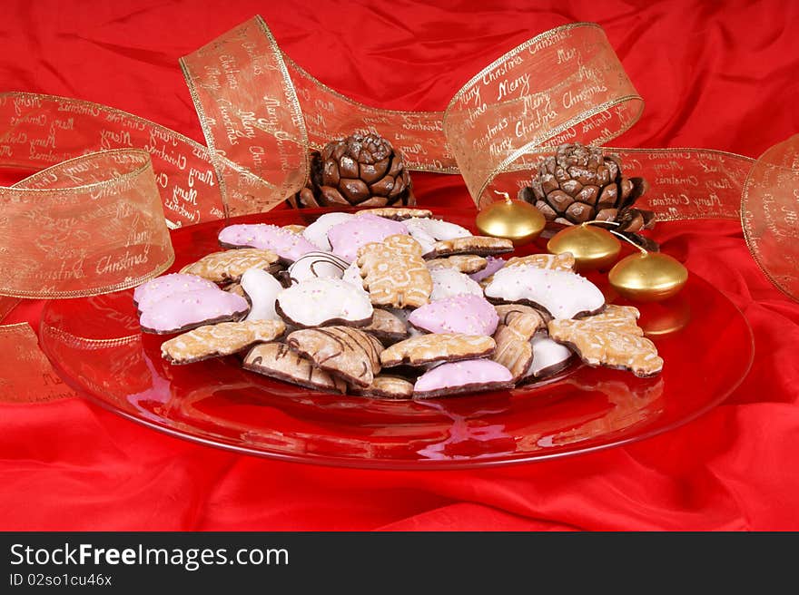 Gingerbread cookies in a red plate with gold candles, pine cones and Christmas ribbon. Studio shot over red background. Gingerbread cookies in a red plate with gold candles, pine cones and Christmas ribbon. Studio shot over red background