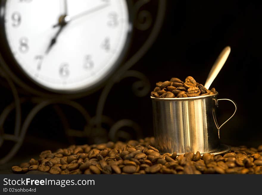 Steel cup of coffee and clock at background