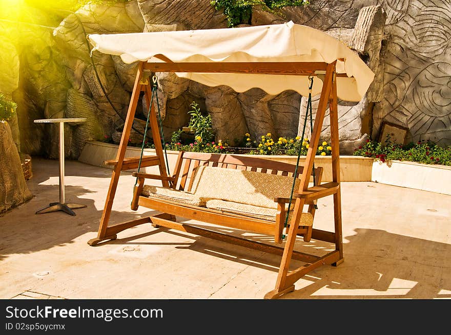 Abandoned splendid wooden swing next to the rock and flowers. Abandoned splendid wooden swing next to the rock and flowers.