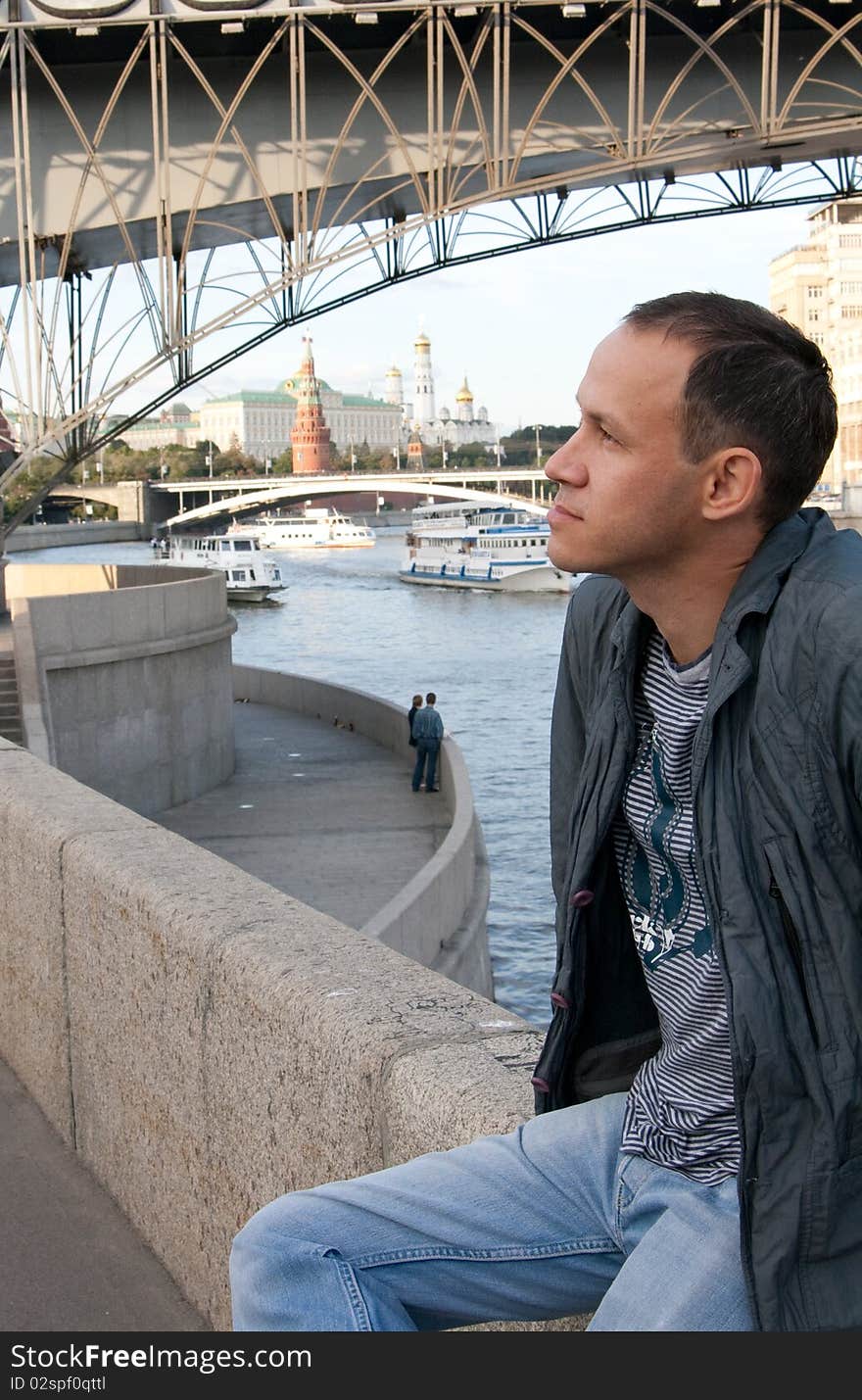 Attractive brunette young man sitting on the barrier near the Moscow river. Attractive brunette young man sitting on the barrier near the Moscow river