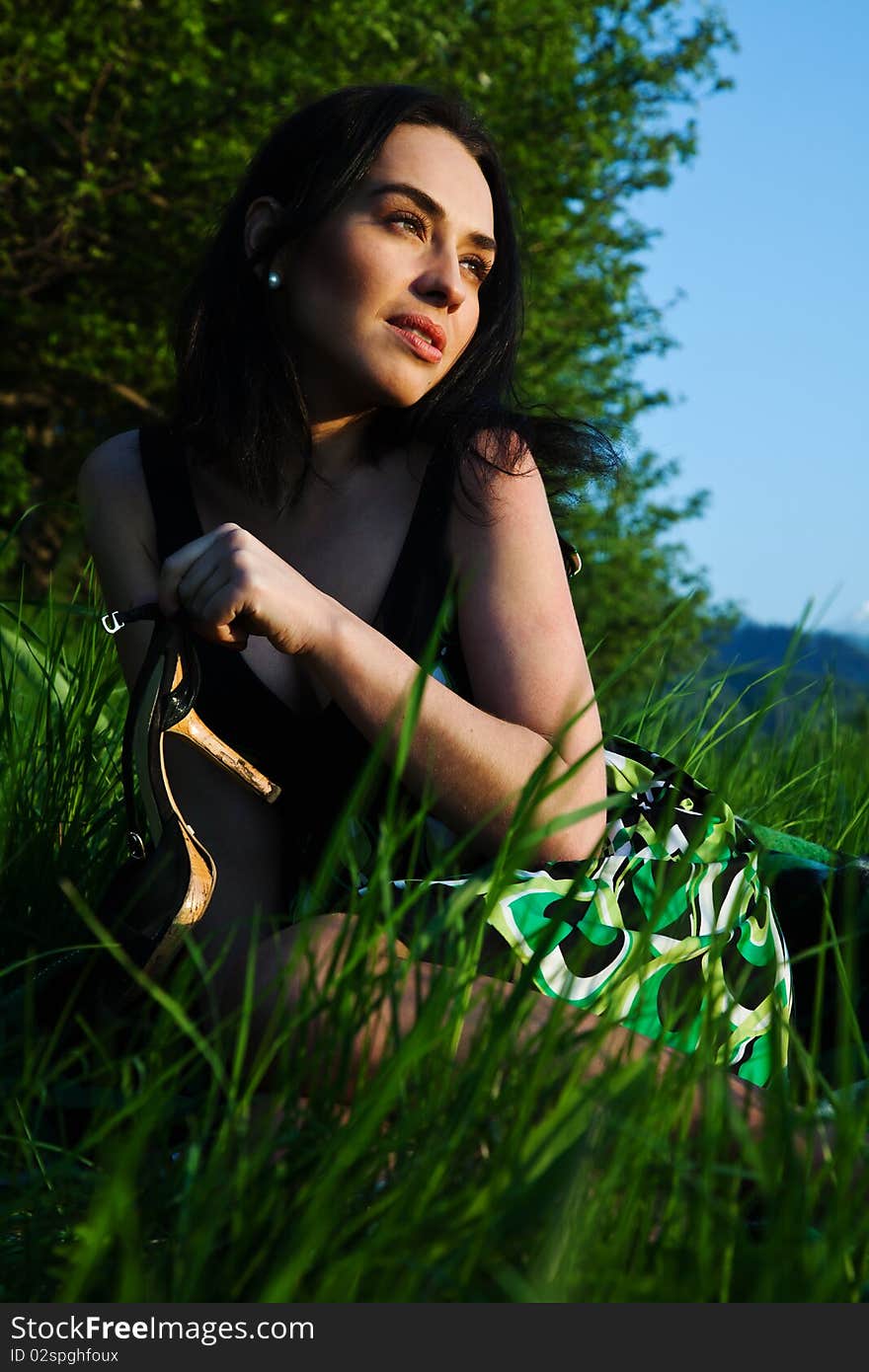 The beautiful girl sits on a green grass, has control over a shoe and thus looks at the sun. The beautiful girl sits on a green grass, has control over a shoe and thus looks at the sun