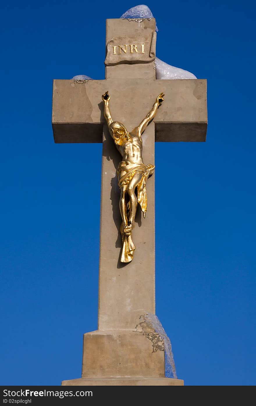 Golden statue of Jesus on a stone cross with a melting snow against a blue sky. Golden statue of Jesus on a stone cross with a melting snow against a blue sky.