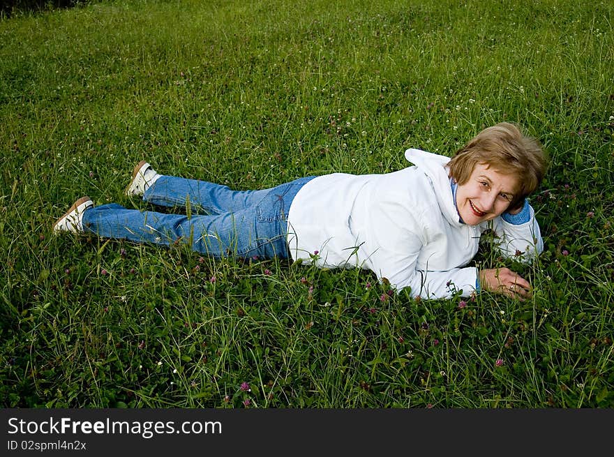 An elderly woman rests on flowering to the meadow. 
Smiles and looks in a photographic camera