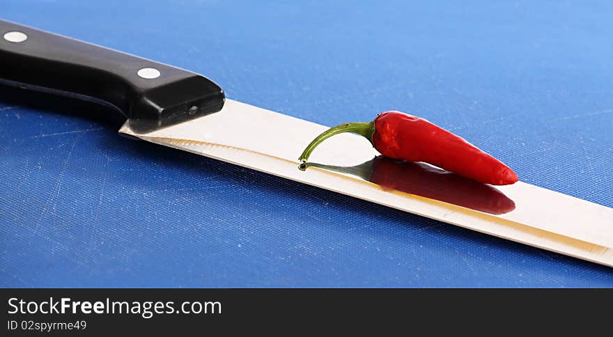 A red hot chili pepper on the blade of a kitchen knife. A red hot chili pepper on the blade of a kitchen knife