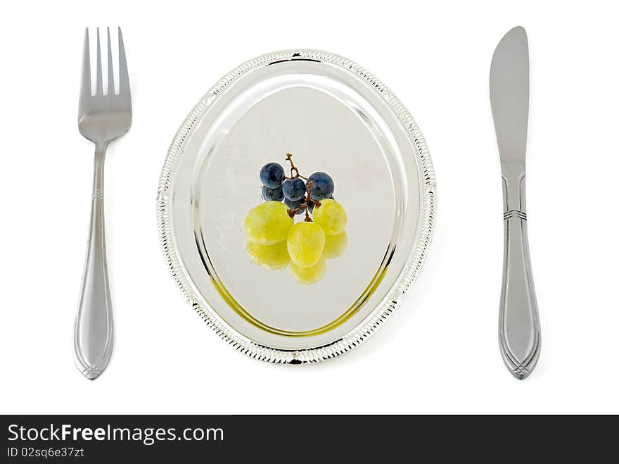 Some berries of a grape lay on a silver plate