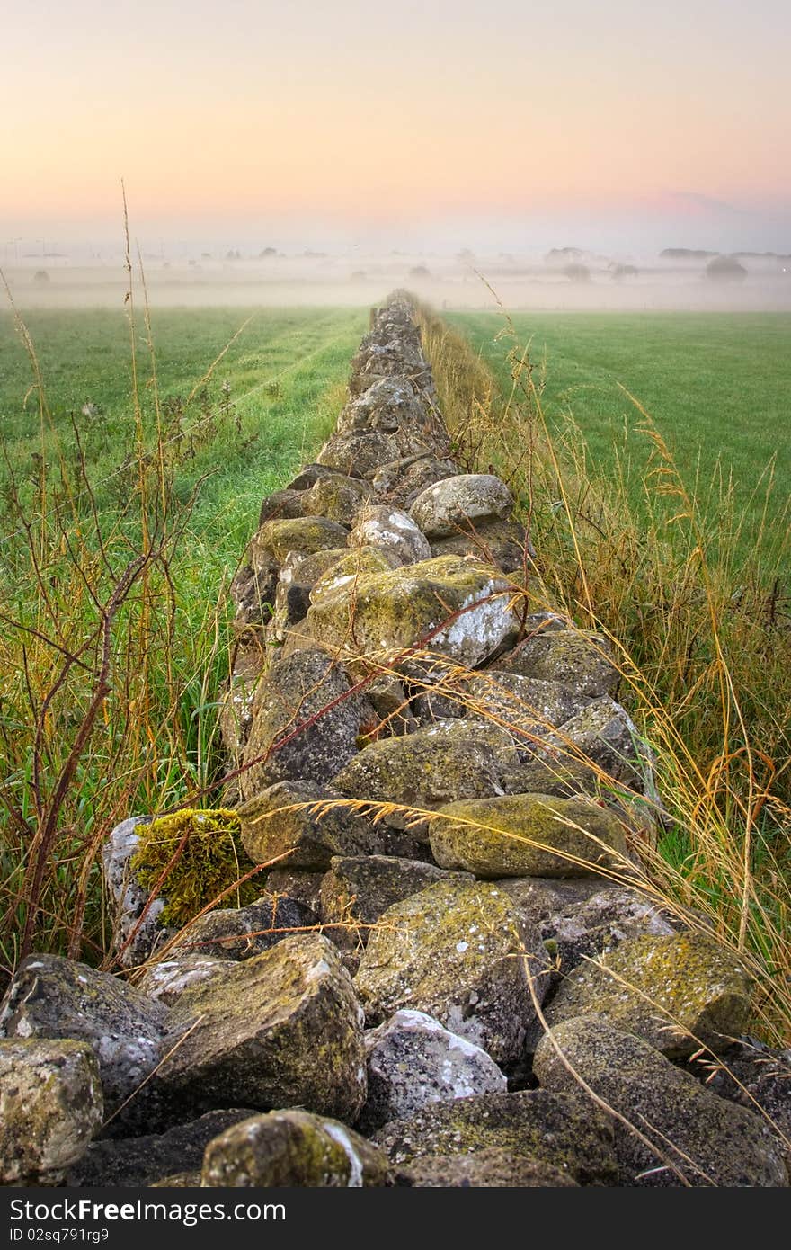 Sunrise and stone wall vanishing in fog, HDR