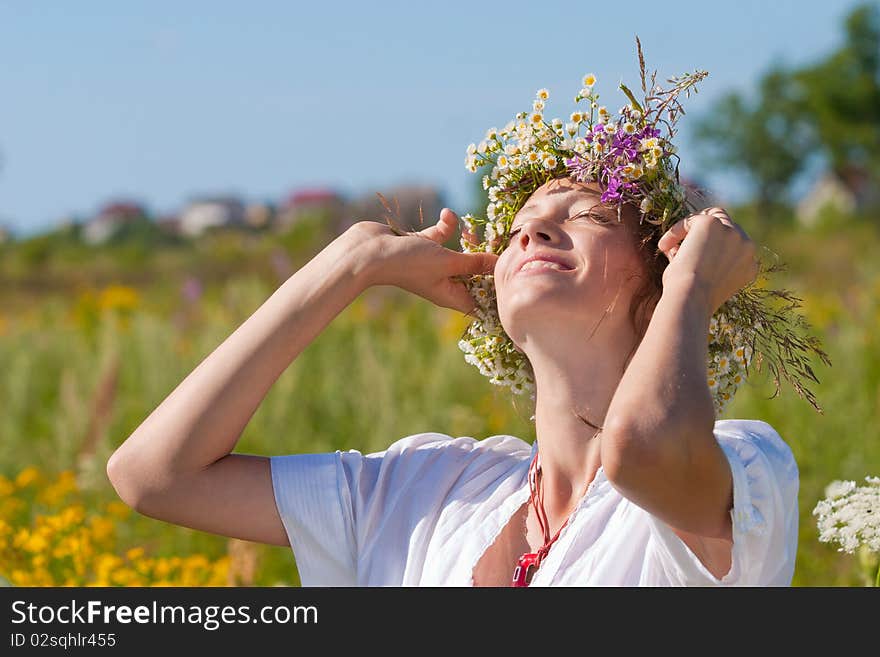 Russian girl in a wreath from camomiles is in a wheaten field