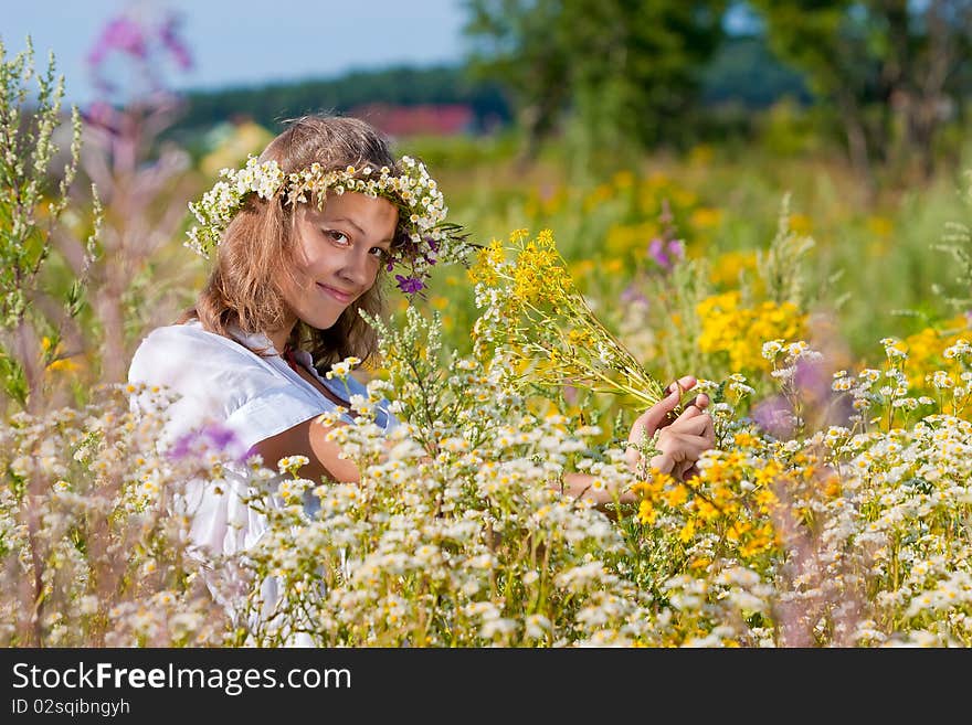 Russian girl in a wreath from camomiles is in a wheaten field