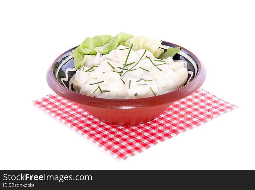 Fresh potato salad in a ceramic dish on a checkered napkin isolated over white