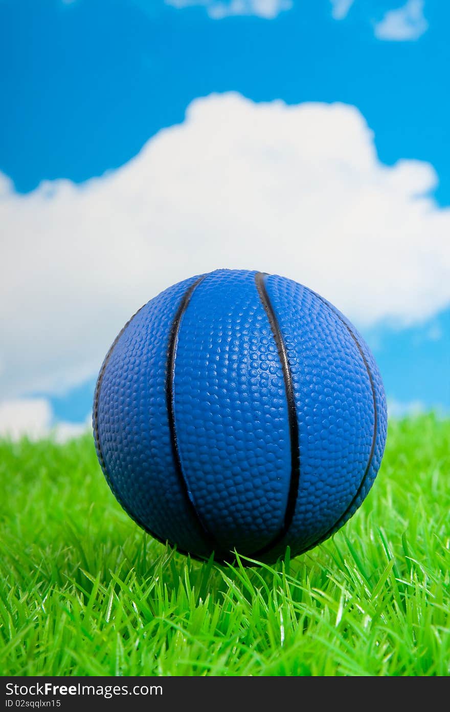 A blue basketball on a green lawn against a blue cloudy sky