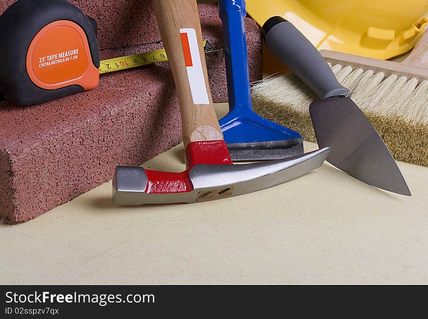 Stonemason's tools next to red bricks on a gray surface.