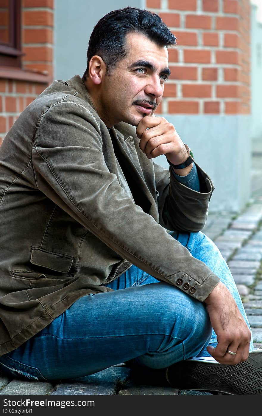 Handsome serious man sitting on street in front of a modern building. Handsome serious man sitting on street in front of a modern building