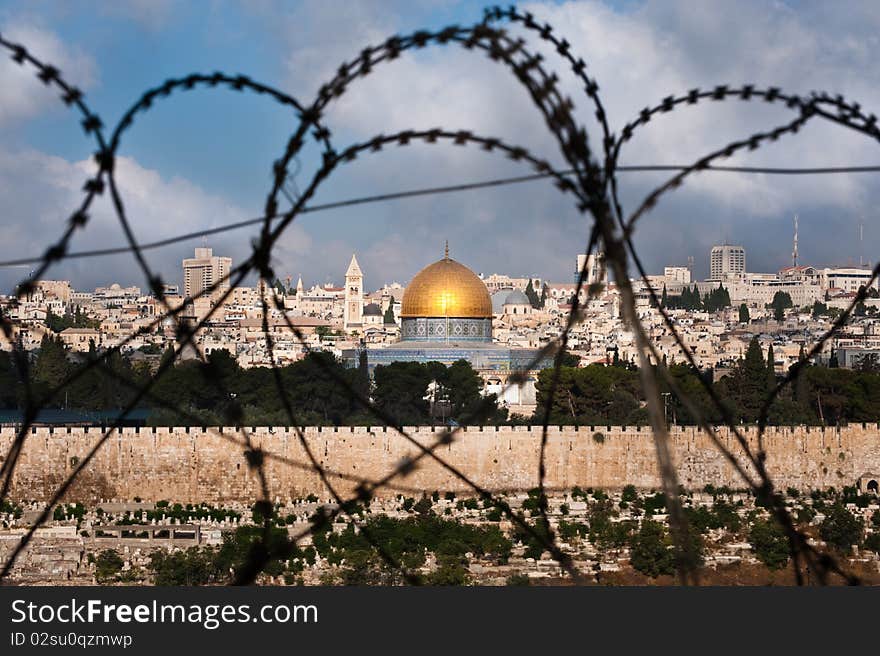 The Old City of Jerusalem, including the Dome of the Rock and various church steeples, seen through coils of razor wire, illustrating the Holy Land's history of division and conflict. The Old City of Jerusalem, including the Dome of the Rock and various church steeples, seen through coils of razor wire, illustrating the Holy Land's history of division and conflict.