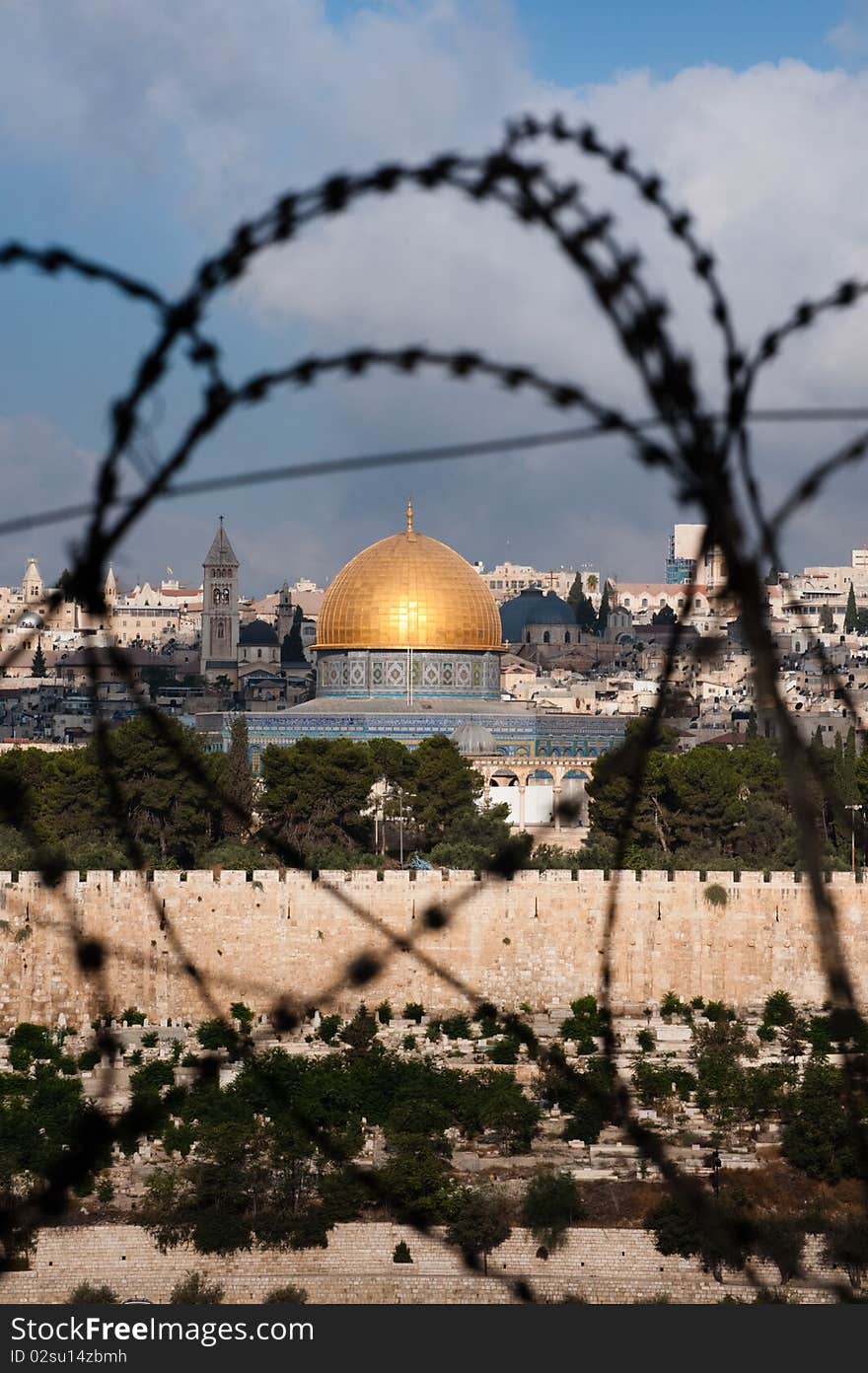 The Old City of Jerusalem, including the Dome of the Rock and various church steeples, seen through coils of razor wire, illustrating the Holy Land's history of division and conflict. The Old City of Jerusalem, including the Dome of the Rock and various church steeples, seen through coils of razor wire, illustrating the Holy Land's history of division and conflict.