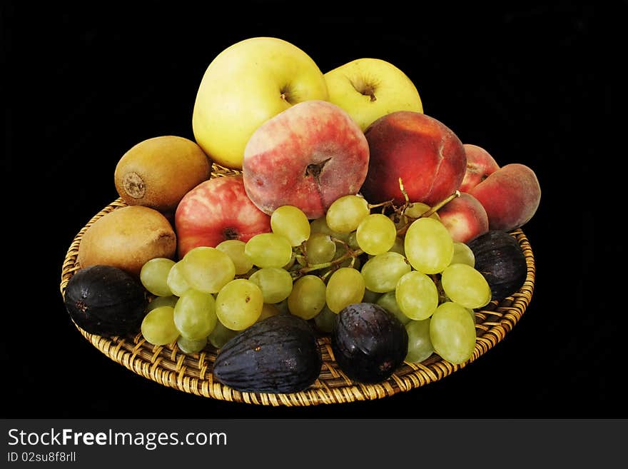 Wicker wooden plate with various fruits in isolated over black. Wicker wooden plate with various fruits in isolated over black