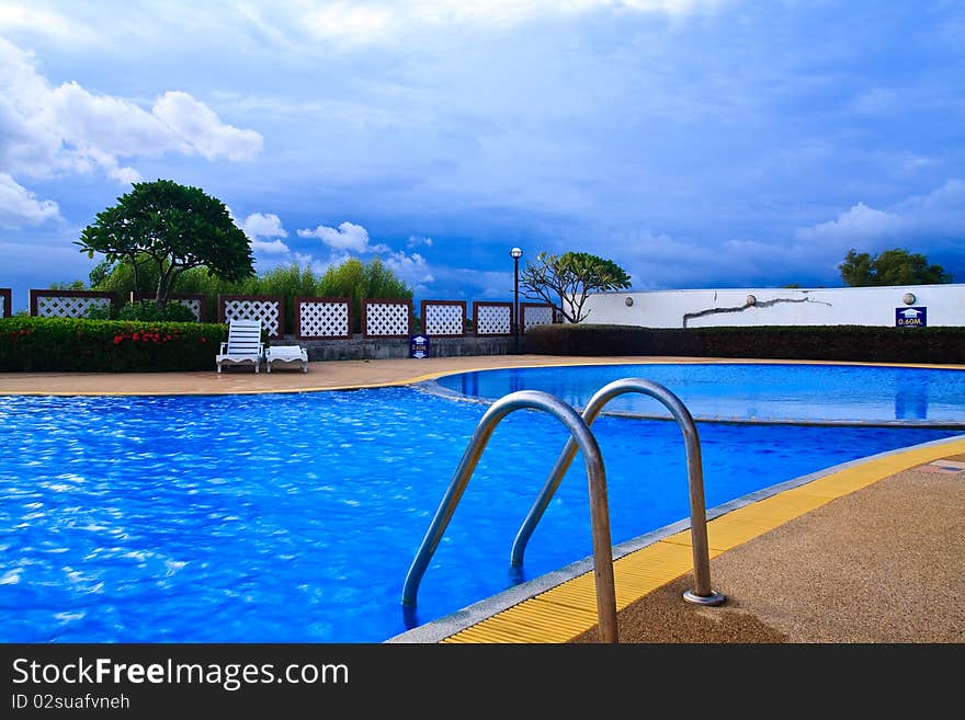 Swimming pool with metallic ladder and blue sky in background. Swimming pool with metallic ladder and blue sky in background