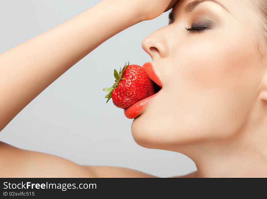 A portrait of a nude woman holding a red-ripe strawberry in her mouth. A portrait of a nude woman holding a red-ripe strawberry in her mouth.