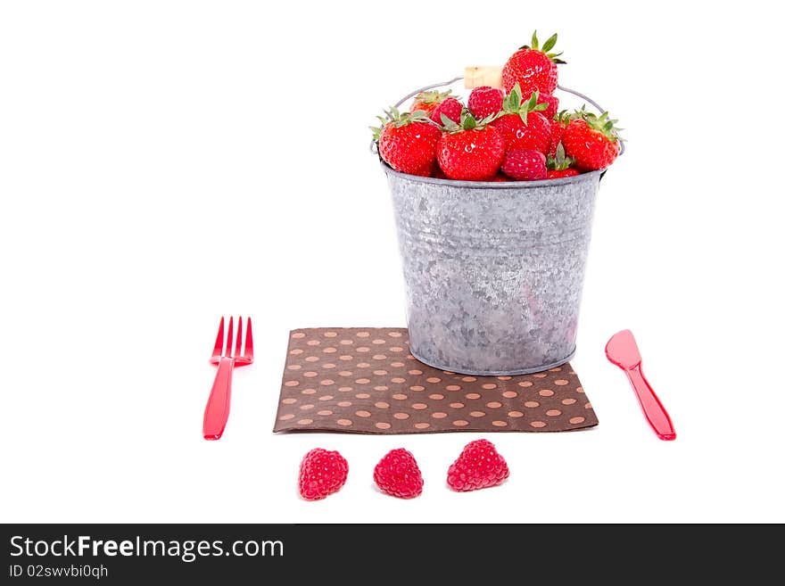 Cutlery with a bucket full of red fruit and a napkin isolated over white