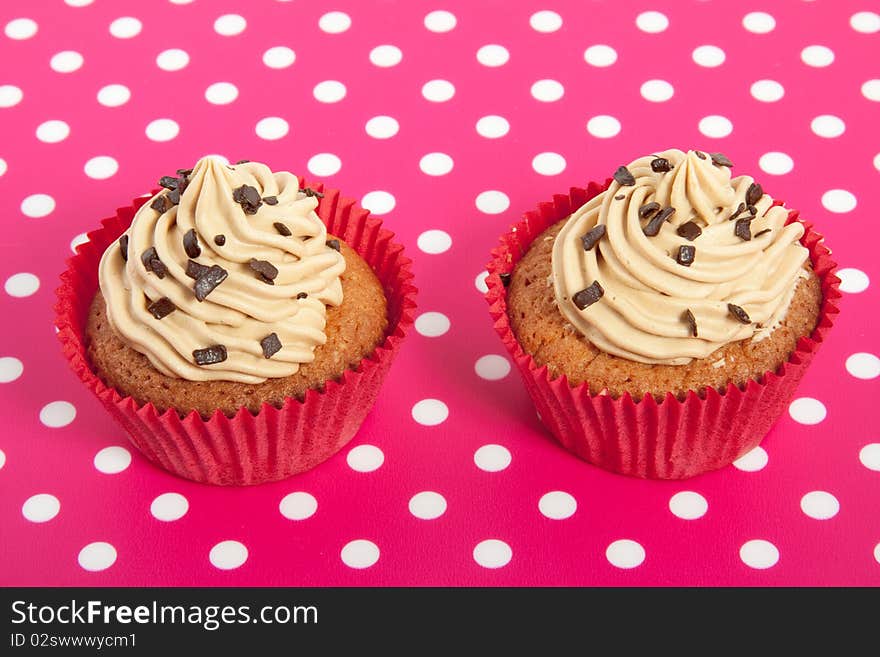 Two red cupakes with cream and chocolate on a pink white dotted background. Two red cupakes with cream and chocolate on a pink white dotted background