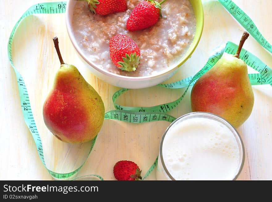 Boiled porridge of oat-flakes with a strawberry by the row of pear, glass of milk. Boiled porridge of oat-flakes with a strawberry by the row of pear, glass of milk