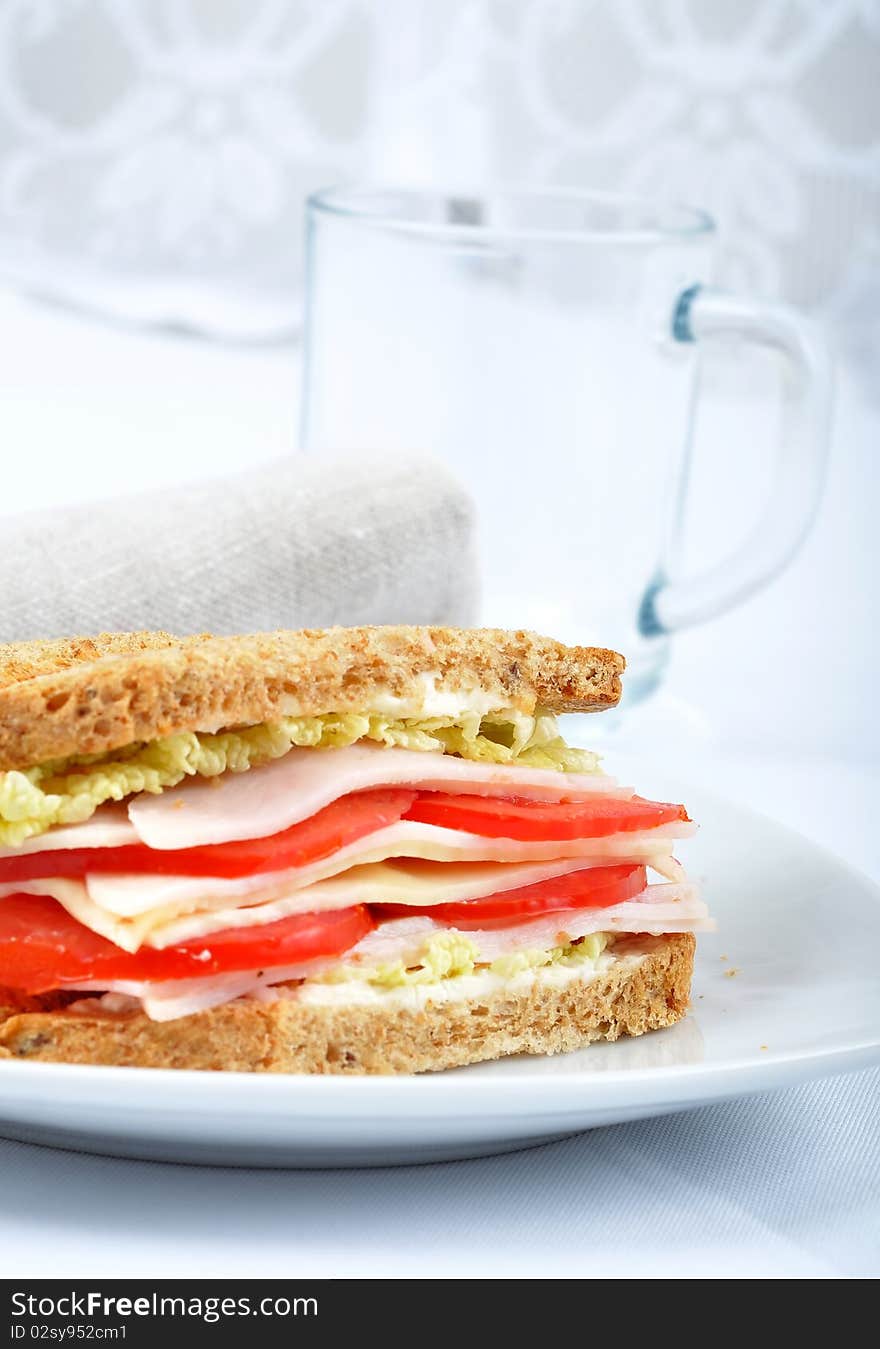 Fresh and delicious classic club sandwich over a white glass dish with glass cup. Fresh and delicious classic club sandwich over a white glass dish with glass cup