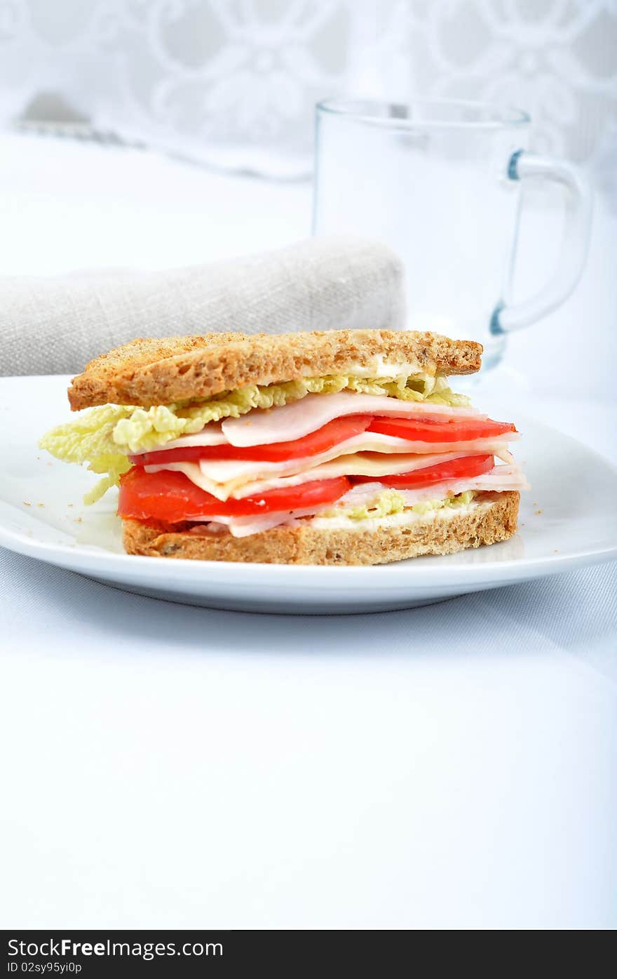 Fresh and delicious classic club sandwich over a white glass dish with glass cup