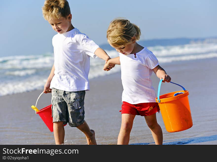 Brother and sister children walk along the ocean edge looking for shells. Brother and sister children walk along the ocean edge looking for shells