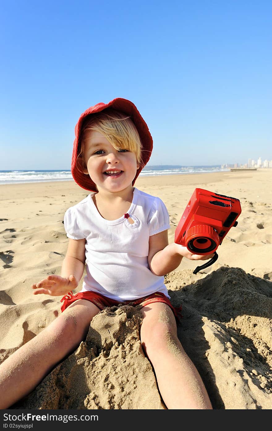 Adorable little girl takes pictures with her red camera on the beach. Adorable little girl takes pictures with her red camera on the beach