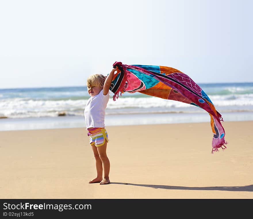 Young cute blonde child on vacation is holding a sarong in the wind. Young cute blonde child on vacation is holding a sarong in the wind