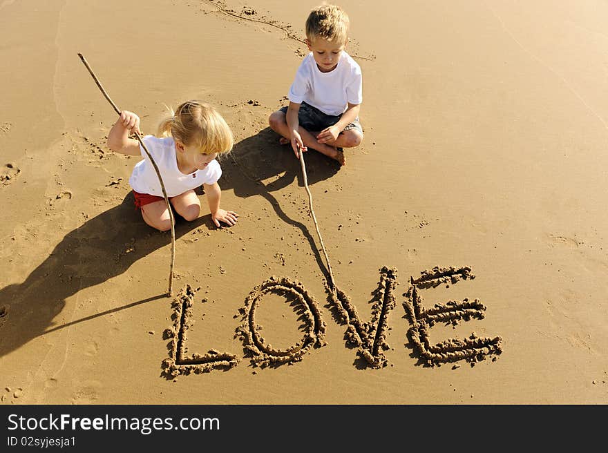 Lovely young brother and sister write words in the sand together. Lovely young brother and sister write words in the sand together