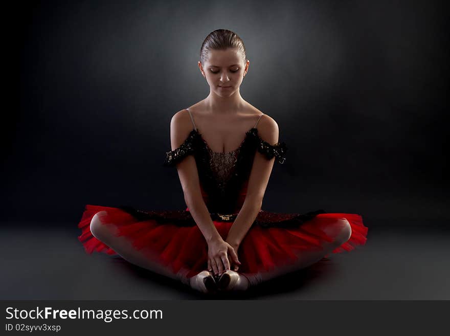 Picture of a beautiful ballerina sitting on a dark background