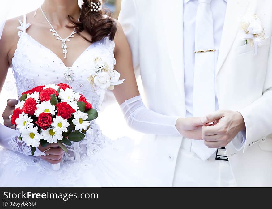 Bridegroom keeping bride hand and beautiful red roses wedding flowers bouquet at background