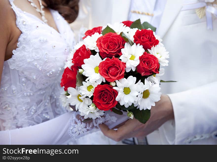 Bridegroom keeping bride hand and beautiful red roses wedding flowers bouquet at background