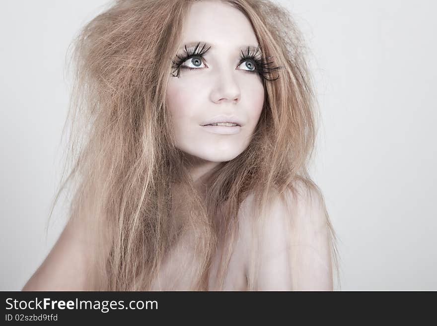 A glamorous, high fashion woman with exaggerated eyelashes and wild hair stares off into distance. Horizontal shot. A glamorous, high fashion woman with exaggerated eyelashes and wild hair stares off into distance. Horizontal shot.