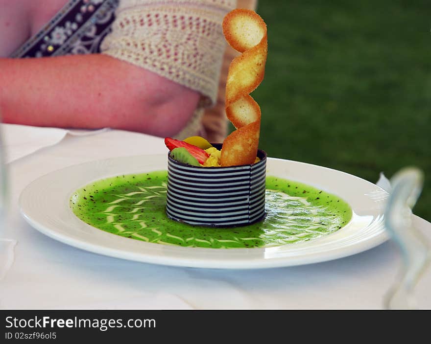 Fruit dessert with green kiwi sauce on white plate