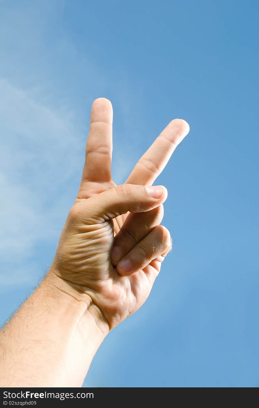 Photo of one hand, which shows the V, against the blue sky. Photo of one hand, which shows the V, against the blue sky