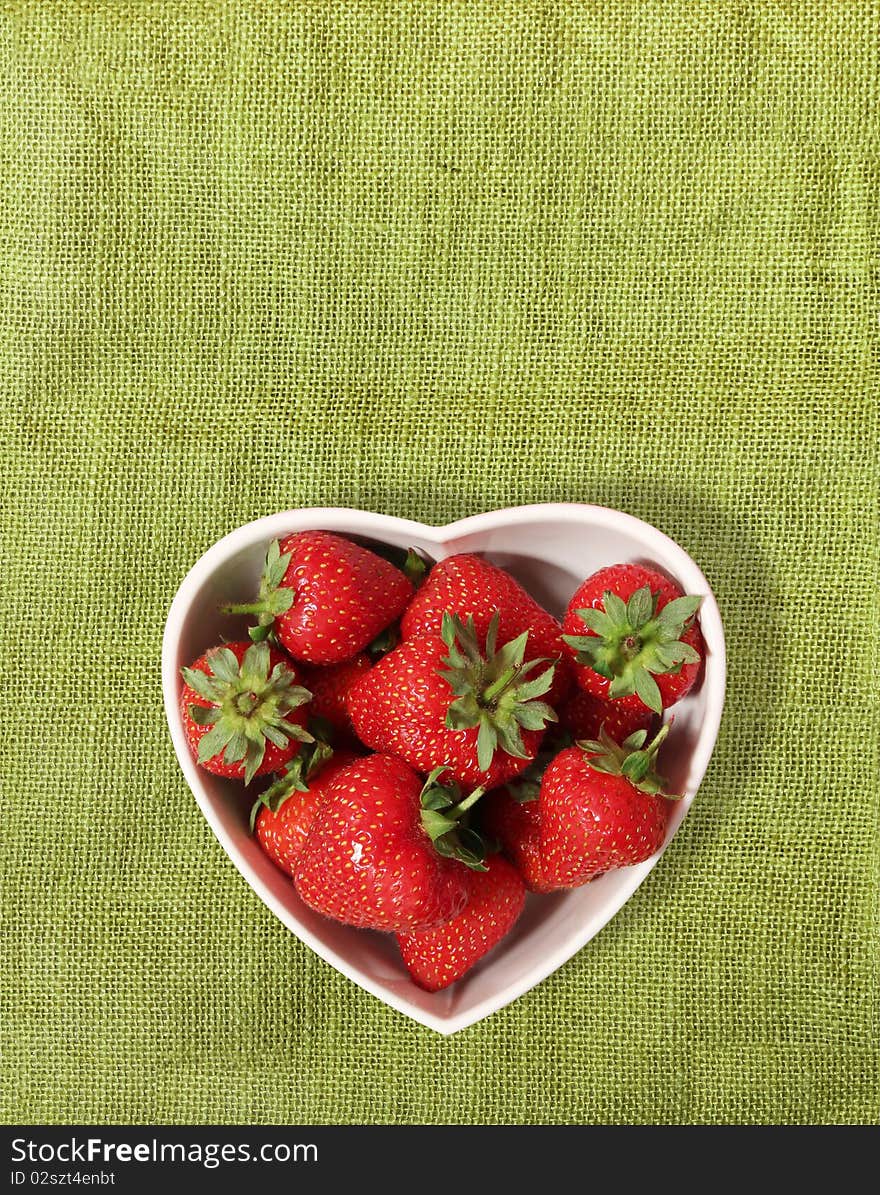 Strawberries in a heart shaped bowl on a green canvas background