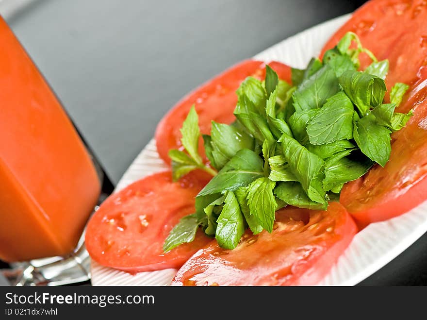 Tomato slices with green leaves and tomato juice in glass on black background